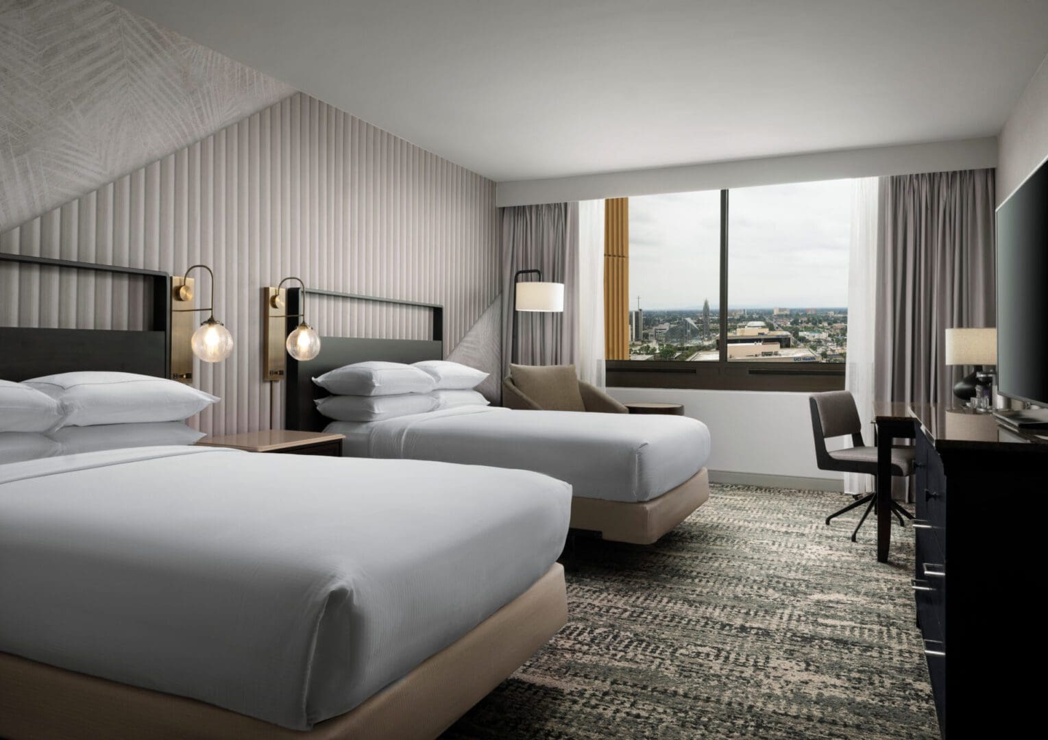 Modern hotel room with two beds and a city view.