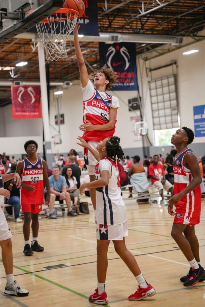 Basketball player performing a slam dunk during a game in a gymnasium.