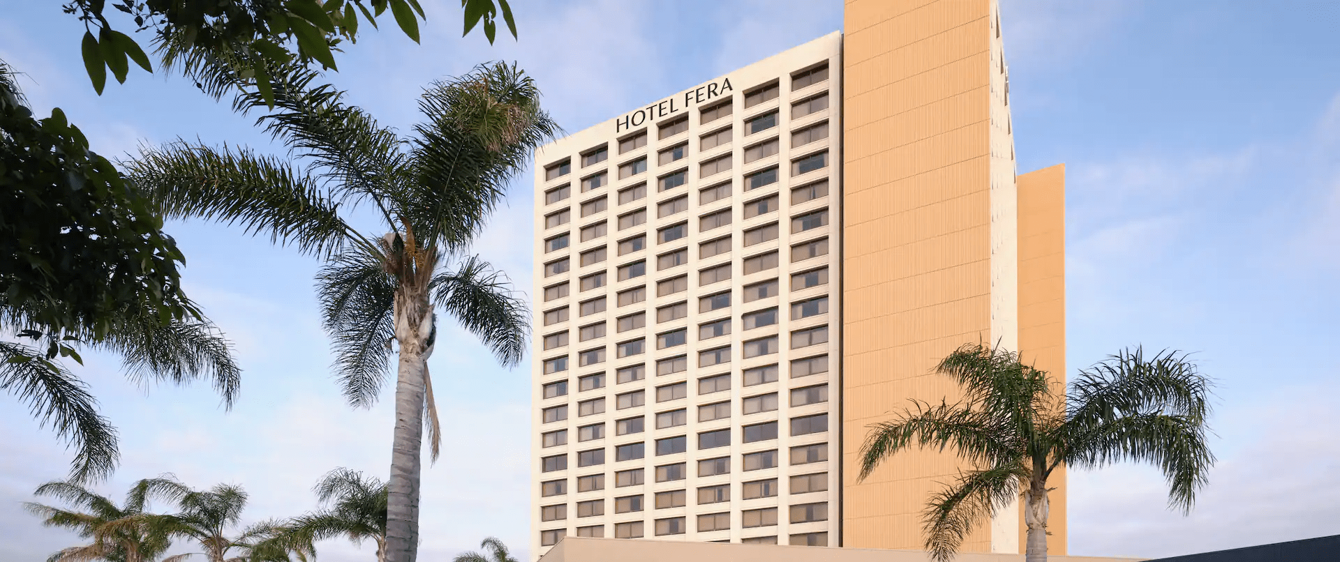 Tall hotel building with palm trees under a clear sky.