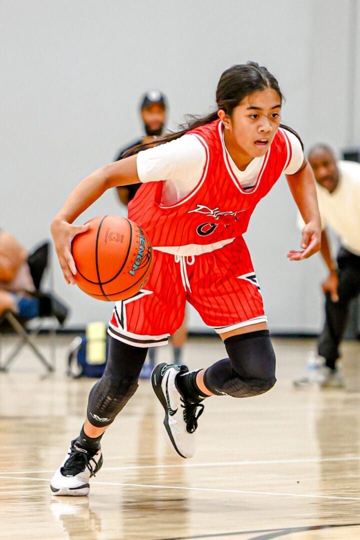 Girl dribbling basketball in red jersey.