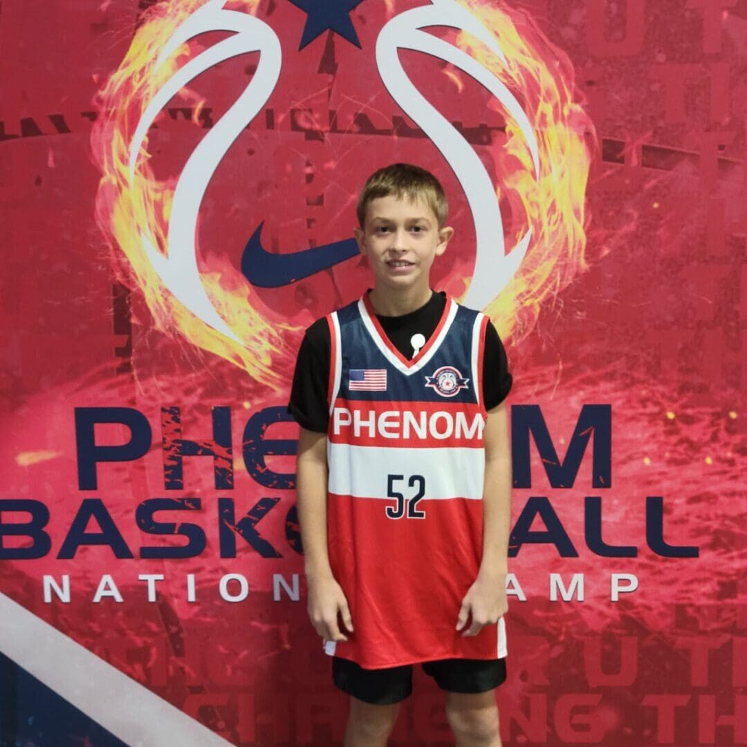 Young basketball player in a red Phenom jersey holding a basketball trophy.